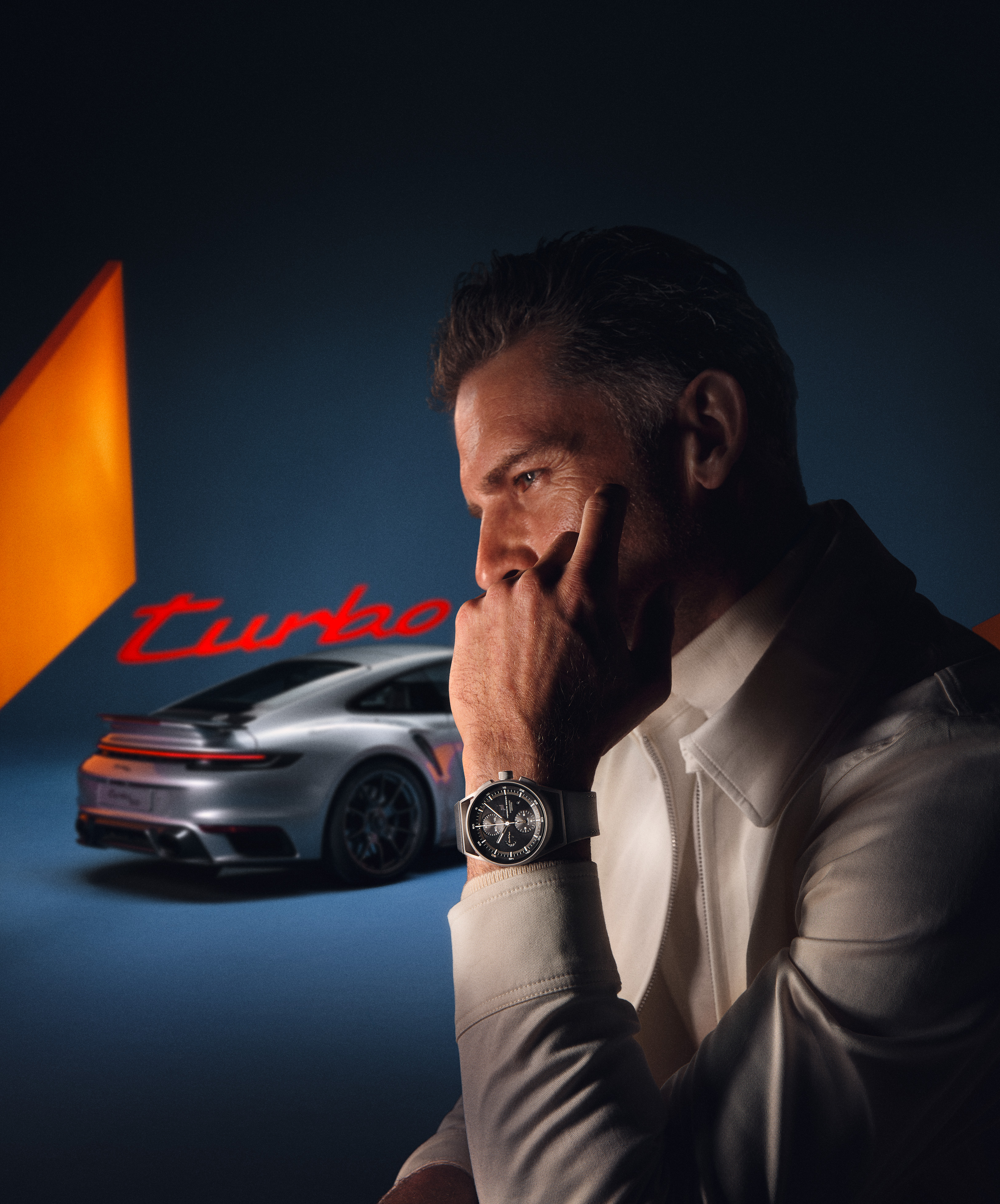 Nahaufnahme eines Mannes mit einem Porsche Design Chronograph 1, der vor einem 911 steht.